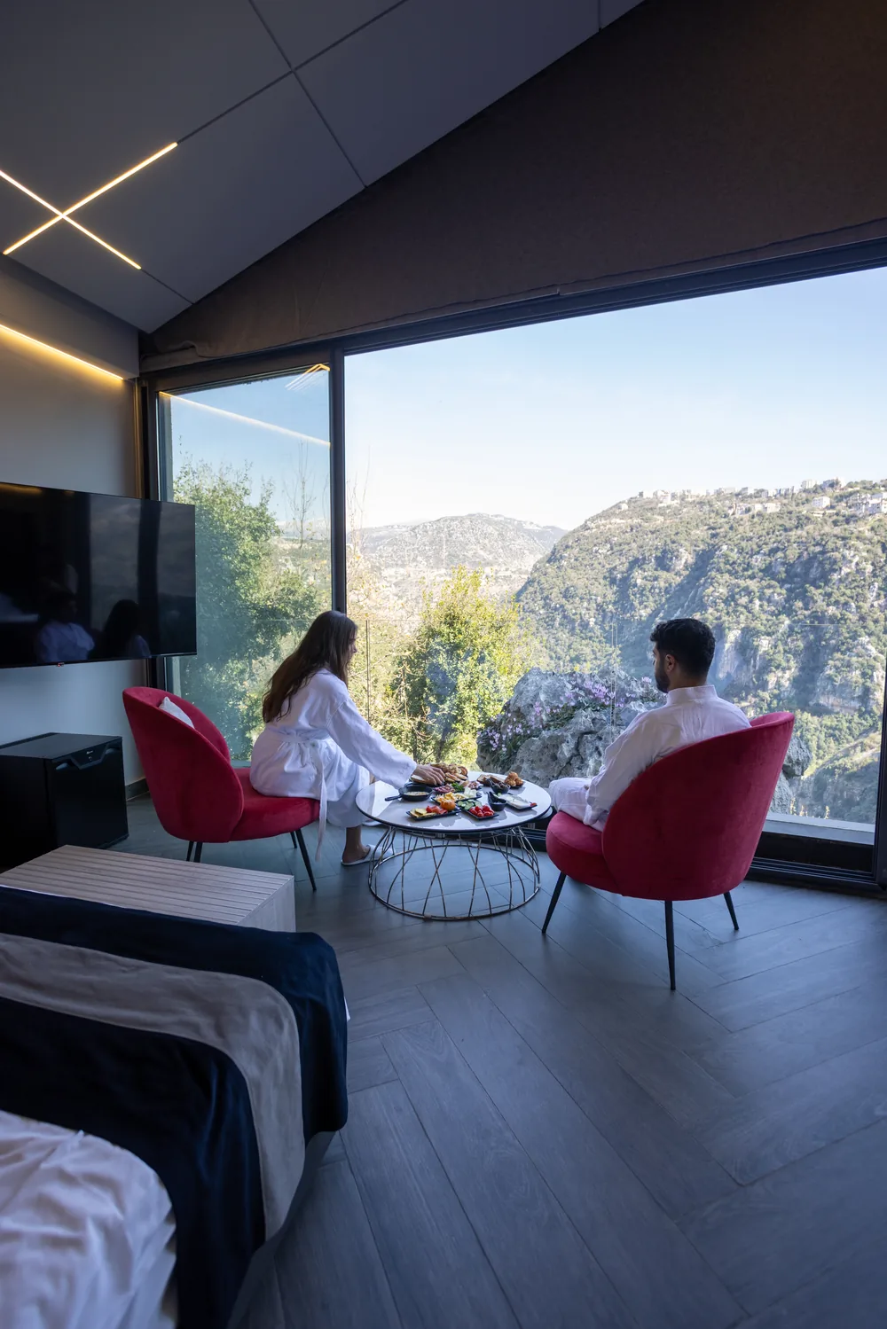 Couple having breakfast in the Flying Room facing the valley through the glass wall